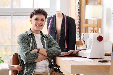 Young male tailor using sewing machine sitting at table in atelier Stock Photos