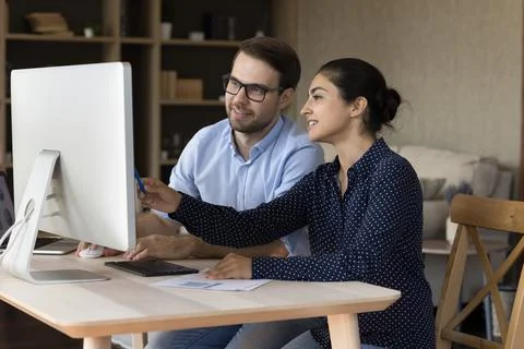 Young male trainee work by computer with Indian female mentor Stock Photos
