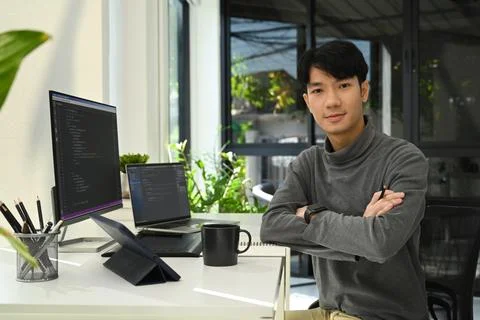 Young male website developer sitting front of computers with coded data on Foto stock