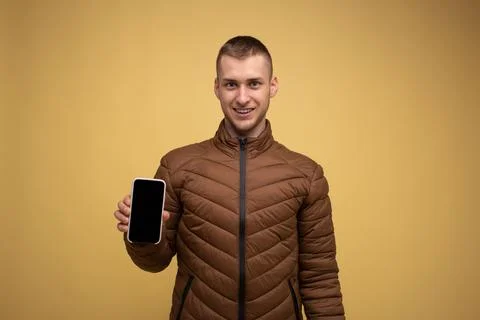 A young man of the 20s in a brown jacket, on a yellow background, holds a mob Stock Photos