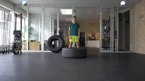 Young man about to flip a big tire during his workout at a cross-training gym Stock Footage 114138909