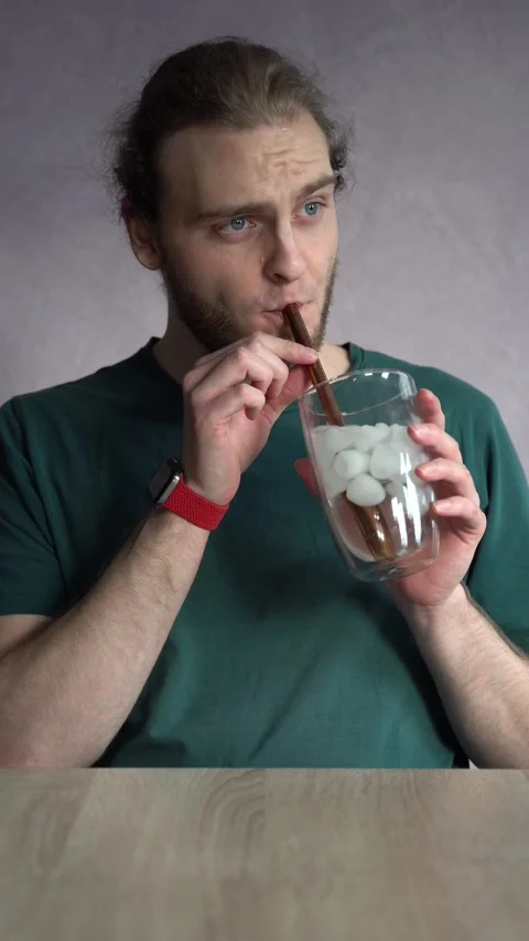 Young man absentmindedly drinking ice water with metal straw Stock Footage 229650844
