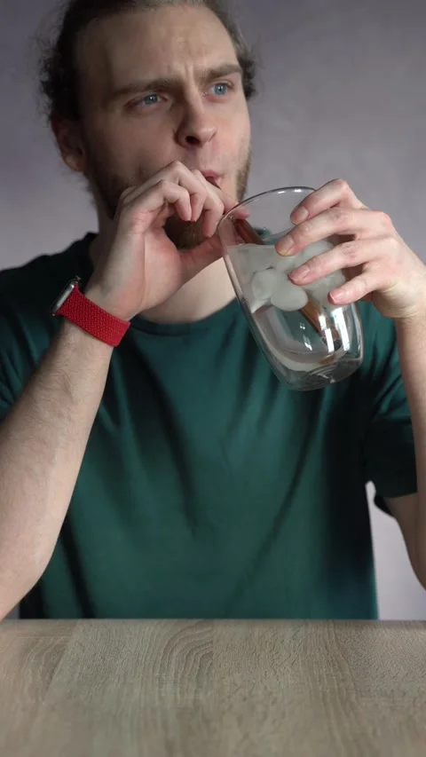 Young man absentmindedly drinking ice water with metal straw Stock Footage 229650867