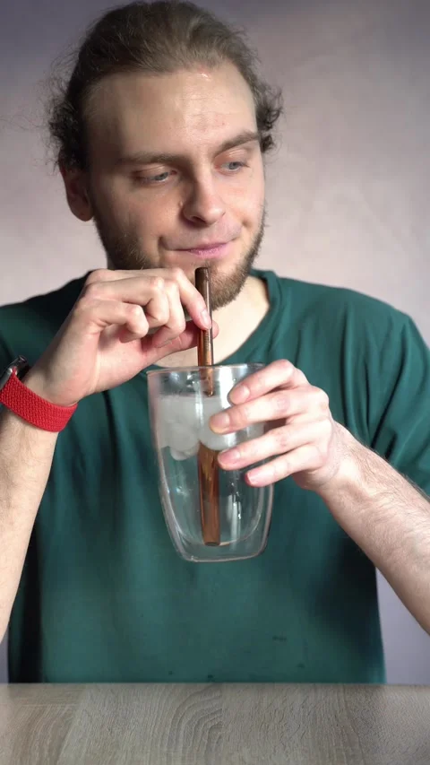 Young man absentmindedly drinking ice water with metal straw Stock Footage 229651035