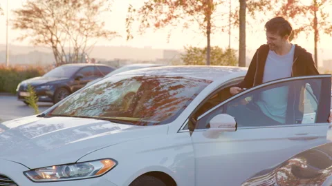 Young man accessing carsharing vehicle in urban setting, surrounded by parked Stock Footage 315532402