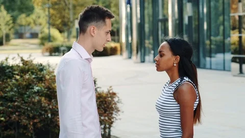 Young man accusing his mixed-race girlfriend of betrayal outdoors Stock Footage 119411001