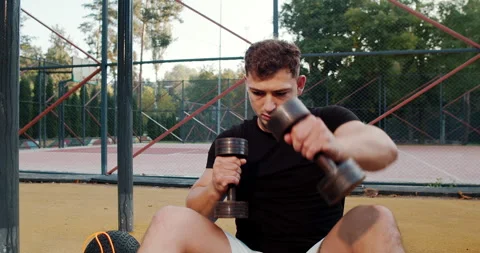 A young man is actively engaged in training with dumbbells in an outdoor gym Stock Footage 317979404