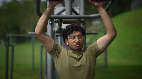 A young man is actively exercising outdoors, making use of pullup bars in a Stock Footage 289913033