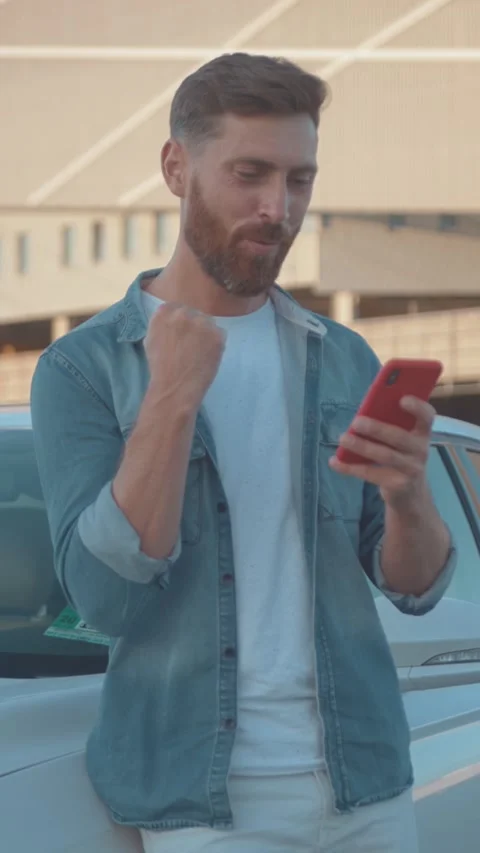 A young man is actively using his smartphone while standing by a modern car in Stock Footage 314959412
