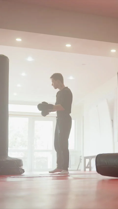 Young Man Adjusting Boxing Gloves Preparing to Punch in Bright Indoor Gym with Stock Footage 343082871