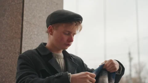 Young man adjusting scarf against textured wall. Young man carefully folding Stock Footage 332919658