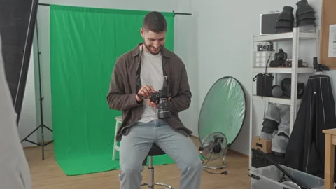 Young man adjusts camera with hands in studio green screen backdrop, sits o.. Stock Footage 337363086