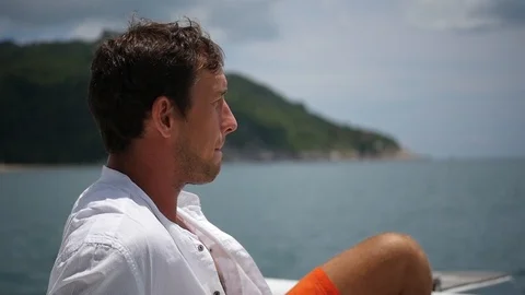 A young man admires the view, sitting on a yacht and drinks clean water from a Stock Footage 94889660