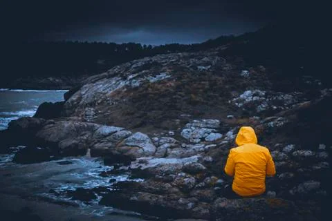 A young man adventurer back shot with contrast yellow jacket sitting over a r Fotos Stock