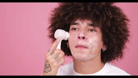 A young man with an afro hairstyle using a circular facial cleansing brush on Stock Footage 269137002