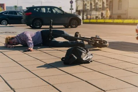 A young man after an accident lying on the road near a scooter Stock Photos