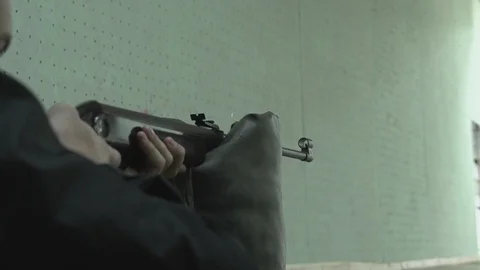 Young man aiming and shooting with a pneumatic rifle lying on the floor in Видео 102779581