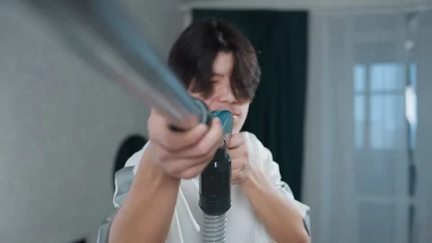 Young man aiming vacuum like rifle with playful expression, closeup angles show Video stock 342336613