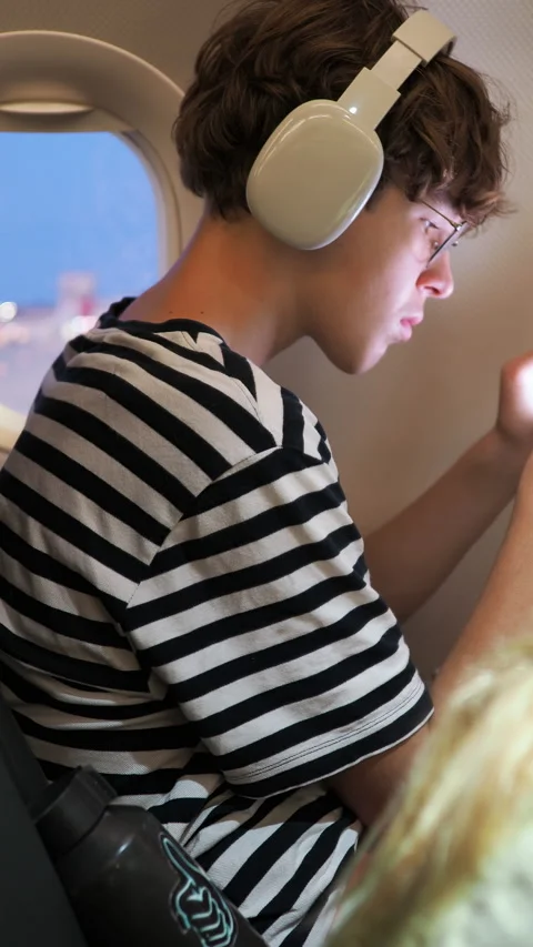 Young Man on Airplane Using Phone with Headphones 库存影片 335389515