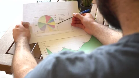 Young man analyzing charts on desk with a computer while investing in stock m Stock Footage 162560954