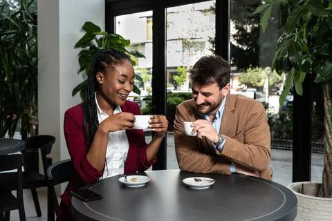 Young man and African American woman sitting in cafeteria drinking coffee f.. Stock Photos
