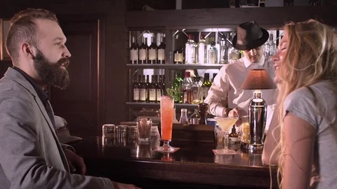 Young man and attractive blonde drinking cocktails in a bar. Bartender in the Stock Footage