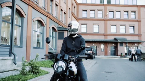 Young man and biker in helmets on motorcycle in city with urban background. Video stock 117974610