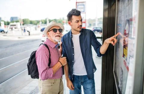Young man and blind senior with white cane at bus stop in city. Stock Photos