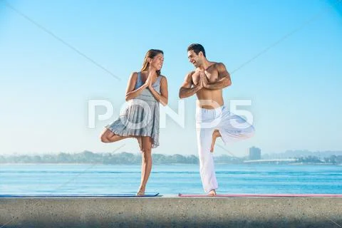 Young Man And Woman Practicing Yoga Position On Pier At Pacific Beach, San