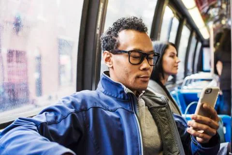 A young man and a young woman sitting on public transport looking at their Stock Photos