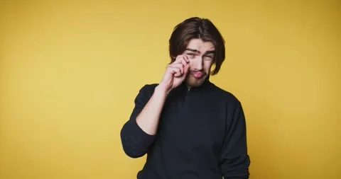 Young man appears contemplative while touching his eye on yellow background Stock Footage 313280323
