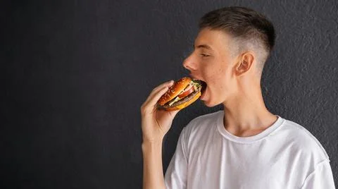 Young man with an appetite eats burger on the street Stock Photos