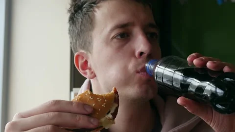 Young man appetizingly eats a juicy tasty hamburger. Junk food alternative Stock Footage 150375565