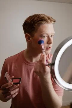 A Young Man Applying Blush In Front Of A Ring Light Mirror Stock Photos