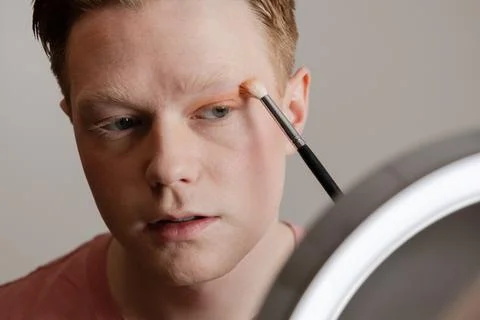 A Young Man Applying Blush In Front Of A Ring Light Mirror Stock Photos