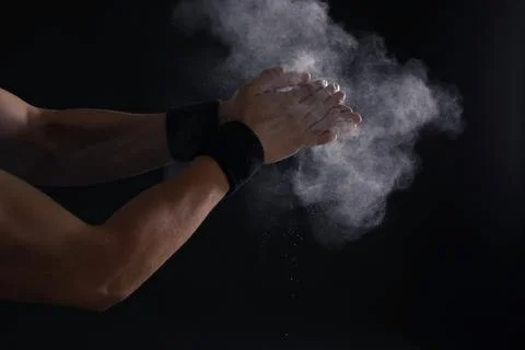 Young man applying chalk powder on hands against dark background Stock Photos