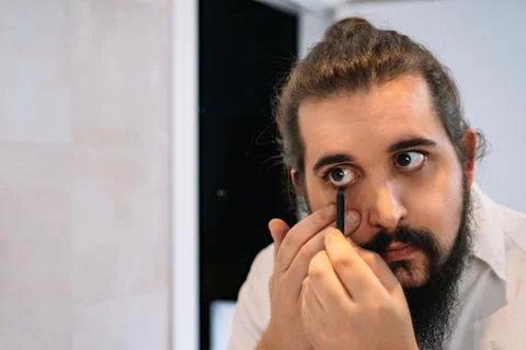 Young man applying eye make-up in the bathroom. Using eyeliner pencil Stock Photos