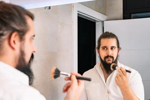 Young man applying make-up in front of the mirror. Daily make-up routine in the Stock Photos