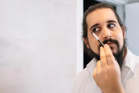 Young man applying make-up in front of the mirror. Daily make-up routine in the Stock Photos