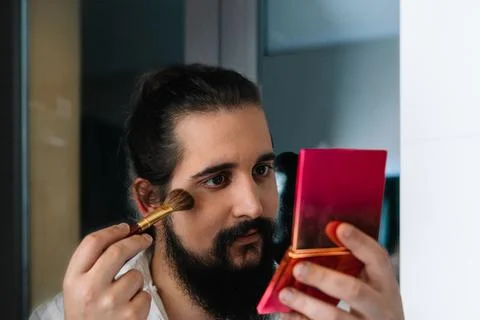 Young man applying make-up in front of the mirror. Daily make-up routine in the Stock Photos