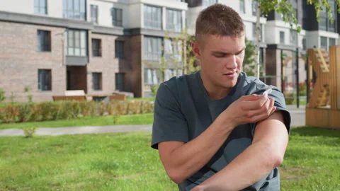Young man applying nicotine patch on arm in green outdoor residential setting Stock Footage 307054835