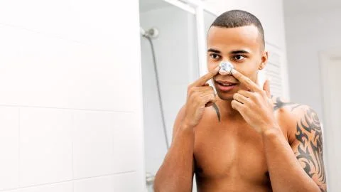 Young man applying nose patch in front of a mirror Stock Photos