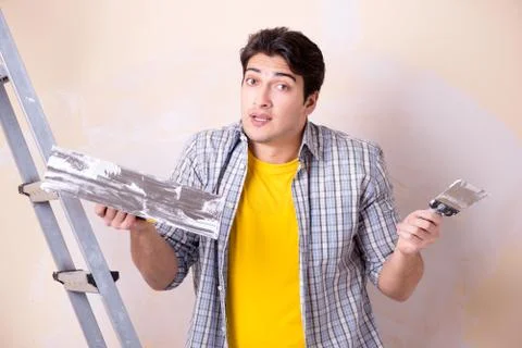 Young man applying plaster on wall at home Fotos Stock