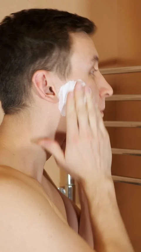 Young man applying shaving cream to face for his morning grooming routine. Daily Stock Footage 344823407