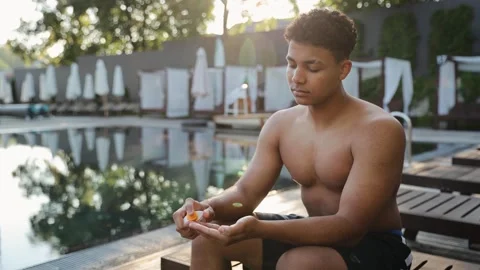 Young man applying sunscreen lotion by pool, preparing for sun protection Stock Footage 328160113