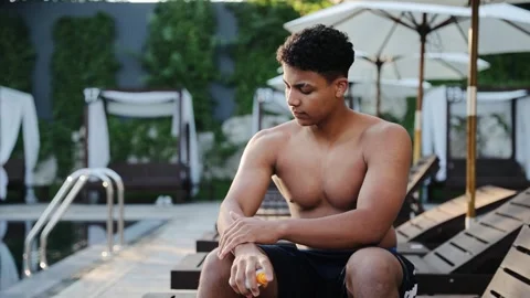 Young man applying sunscreen lotion on hand for sun protection near poolside Stock Footage 333565009