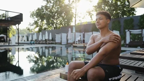 Young man applying sunscreen protecting skin from sun at outdoor swimming pool Stock Footage 333564984