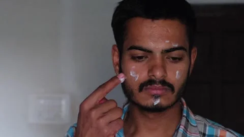 Young man applying white face cream or moisturizer on his face for skin care Stockbeeldmateriaal 330179646