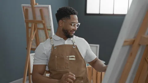 Young man in apron painting at studio and then leans back with hands behind.. Vídeos de archivo 337439157