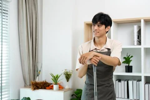Young Man in Apron Smiling While Cleaning Home with Mop in Modern Living Room Stock Photos